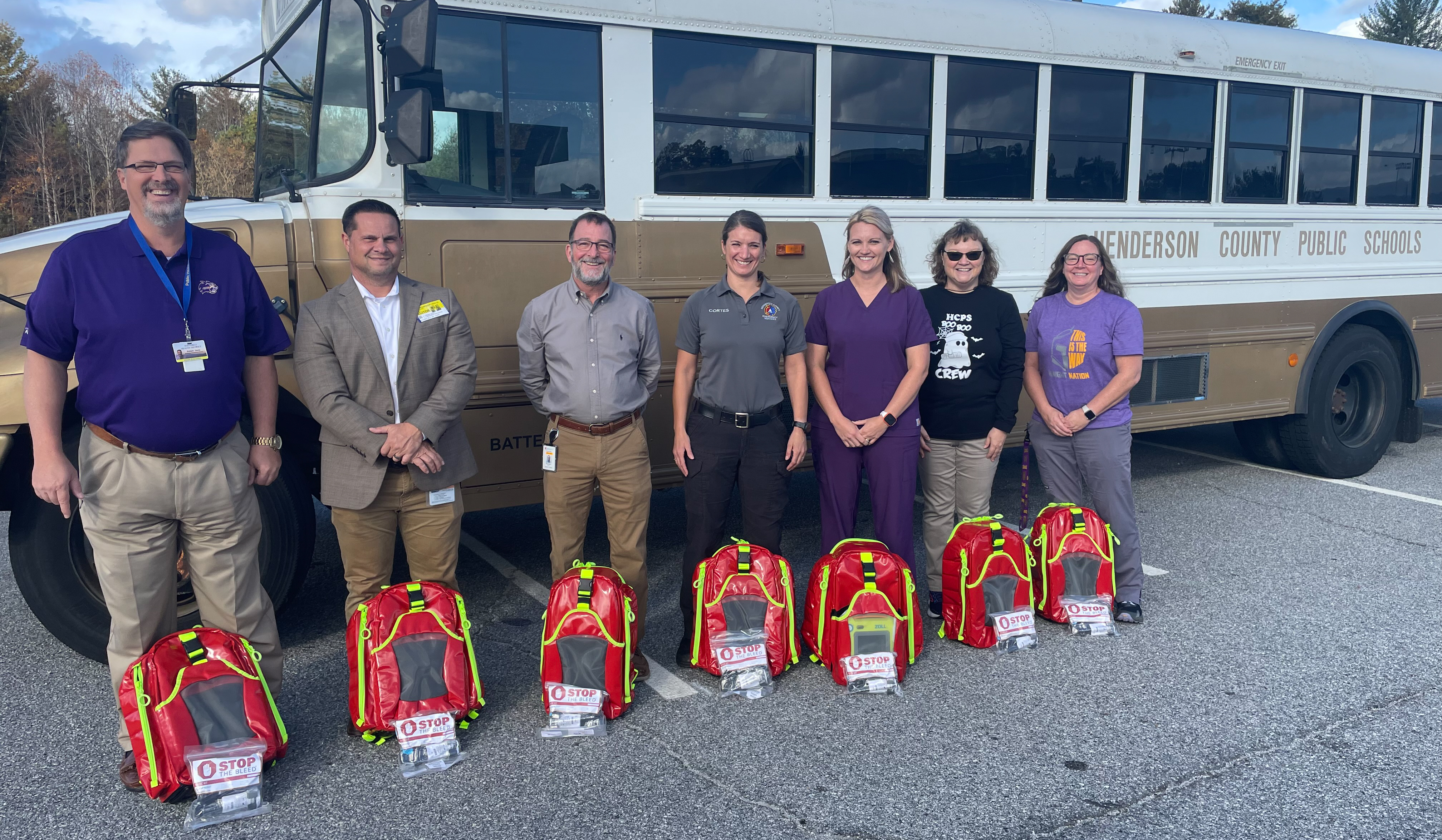 Picture of officials standing with new school nurse response bags in front of a school bus