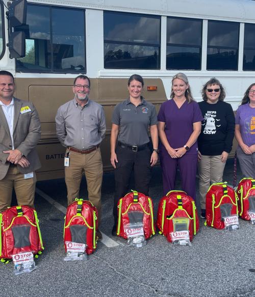 Picture of officials standing with new school nurse response bags in front of a school bus